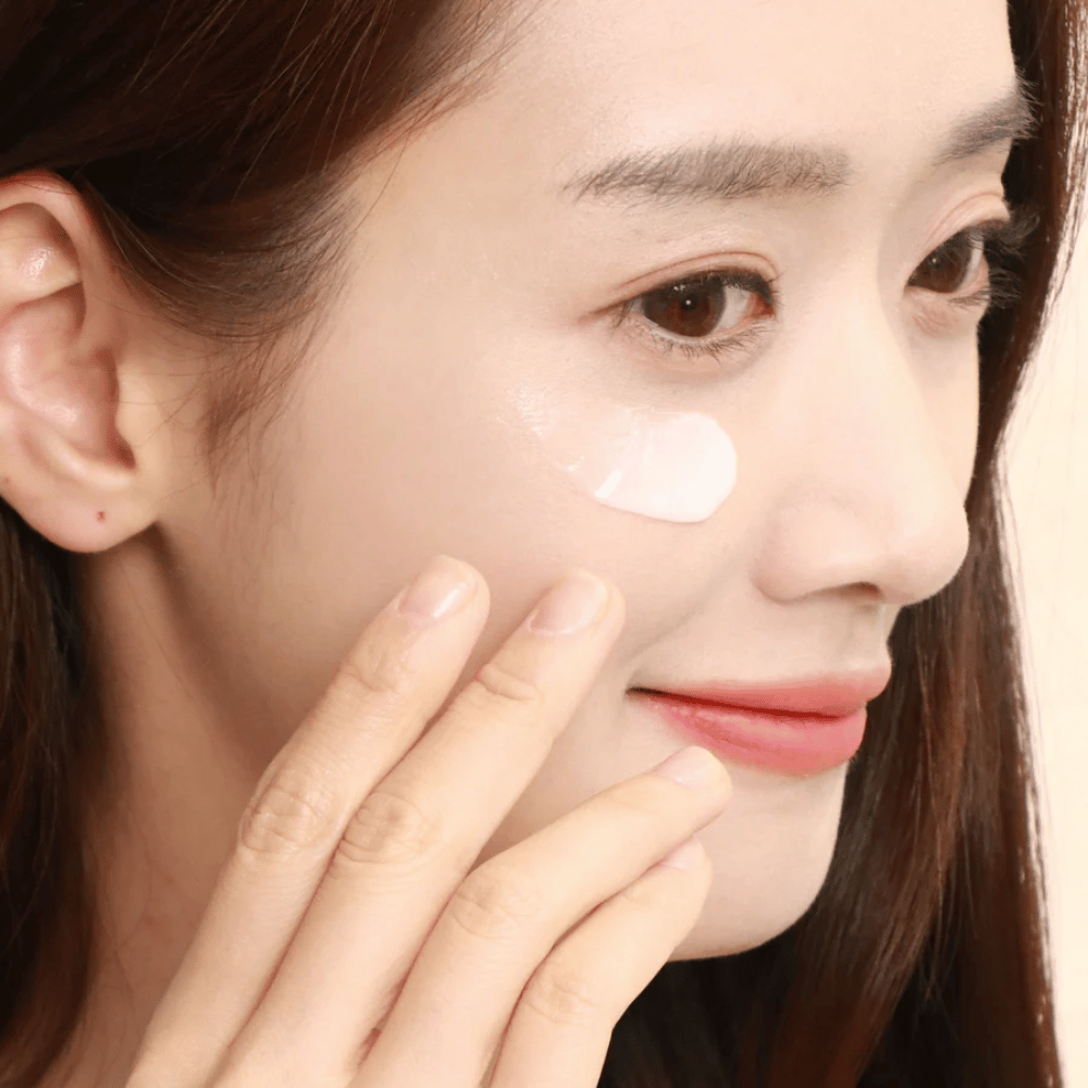 Mujer aplica crema para ojos debajo del ojo con las yemas de los dedos - primer plano que muestra cómo el producto se masajea suavemente en la piel para hidratación y cuidado.