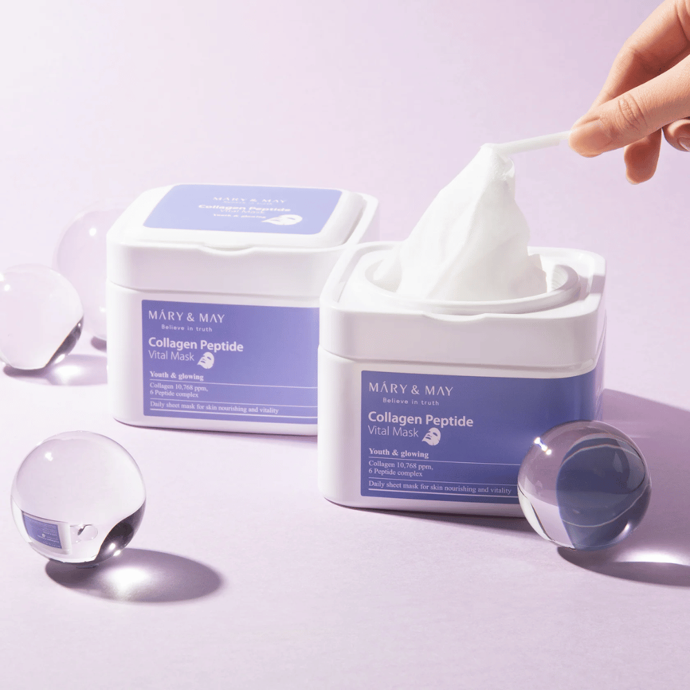 Una mano saca una máscara de un frasco de MARY & MAY Collagen Peptide Vital Mask. La máscara está destinada para uso diario para nutrir y dar brillo a la piel, con colágeno y péptidos para apoyar la juventud de la piel.