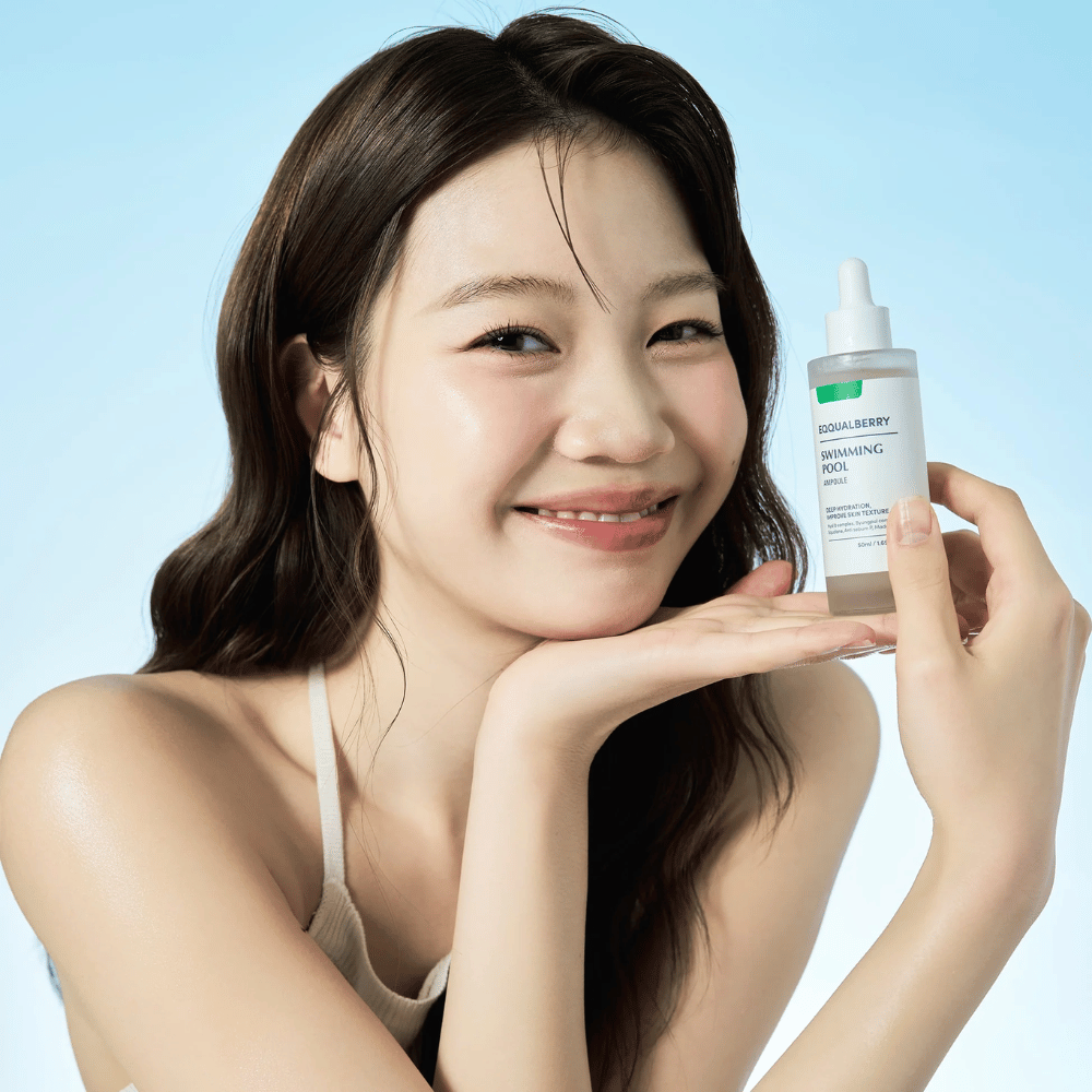 Mujer sonriente que sostiene Eqqualberry Swimming Pool Ampoule, un producto para el cuidado de la piel hidratante, con ambas manos frente a un fondo azul claro.