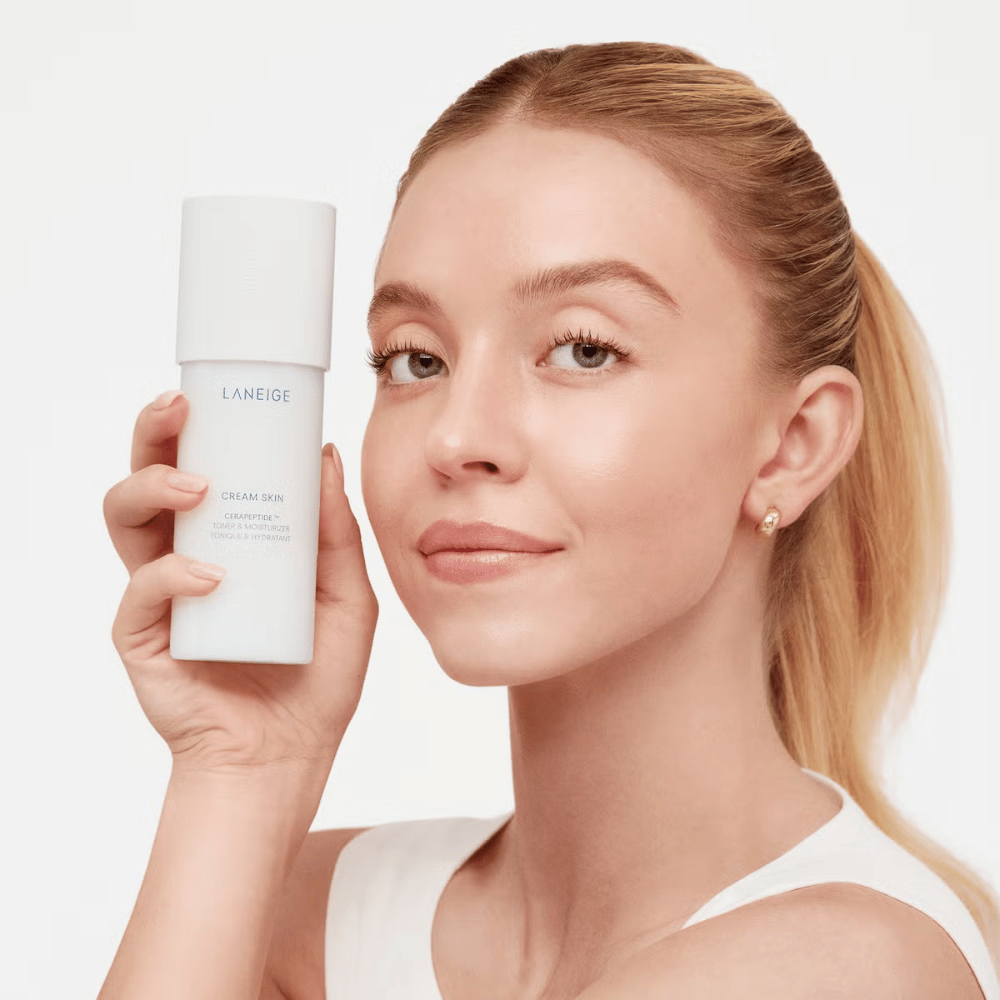 Una persona sostiene Laneige Cream Skin Cerapeptide Refiner en un frasco blanco. La persona sonríe y muestra el producto, que se comercializa como un tónico hidratante y producto de cuidado de la piel.