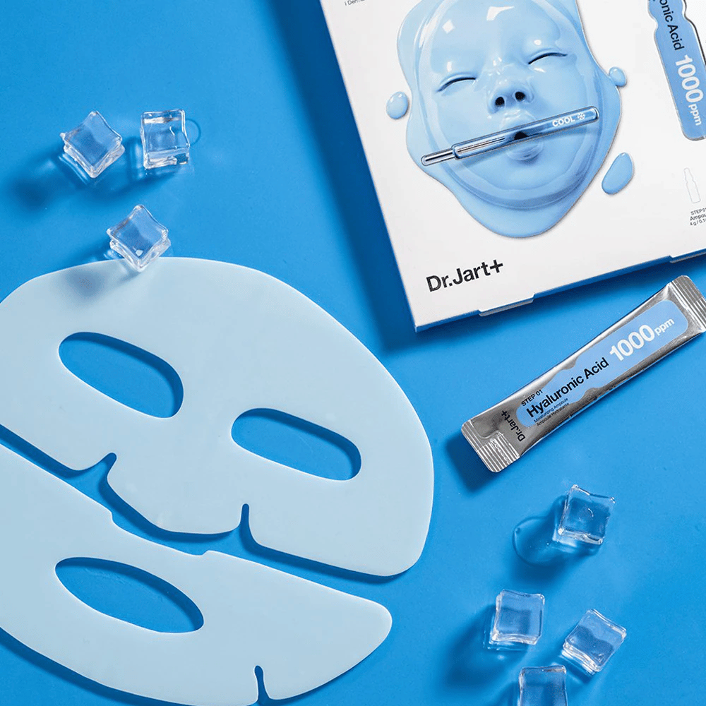 Dr.Jart+ Cryo Rubber Moisturizing Mask con máscara de goma azul de dos partes, cubitos de hielo, ampolla de ácido hialurónico y embalaje sobre fondo azul.