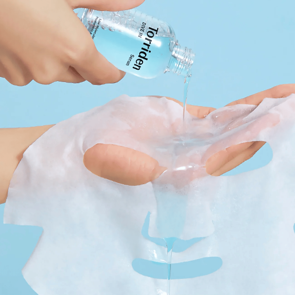 Mascarilla facial dr empapada con solución de una botella "Torriden Dive-In", contra un fondo azul.