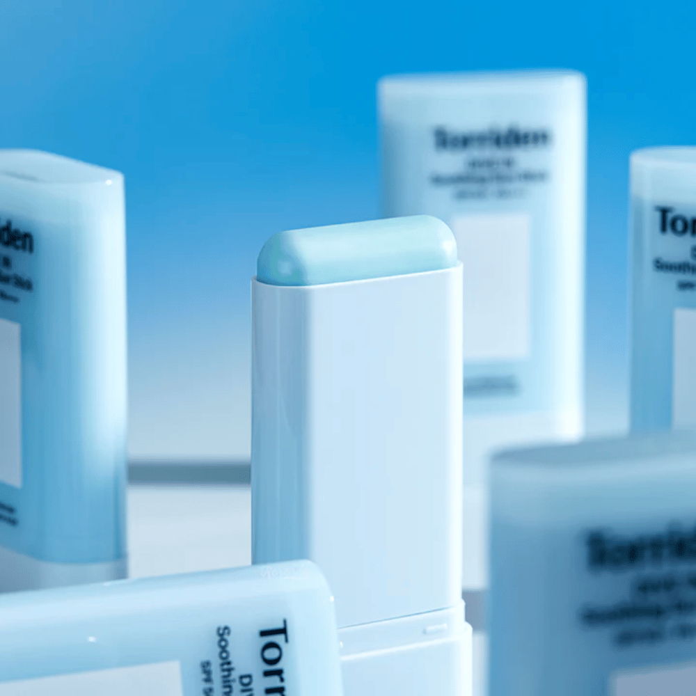 Primer plano de Torriden DIVE IN Soothing Sun Stick que muestra la suave fórmula de protector solar en formato de barra con varios productos al fondo.