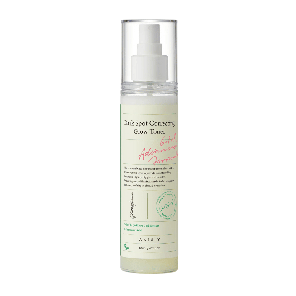 Una imagen de una botella del producto "AXIS-Y Dark Spot Correcting Glow Toner". La botella es transparente con una etiqueta blanca y texto en negro y verde. El producto es un tónico en forma de spray, y la botella contiene 125 ml (4,23 fl. oz). La etiqueta menciona ingredientes clave como Extracto de Corteza de Sauce y Ácido Hialurónico.