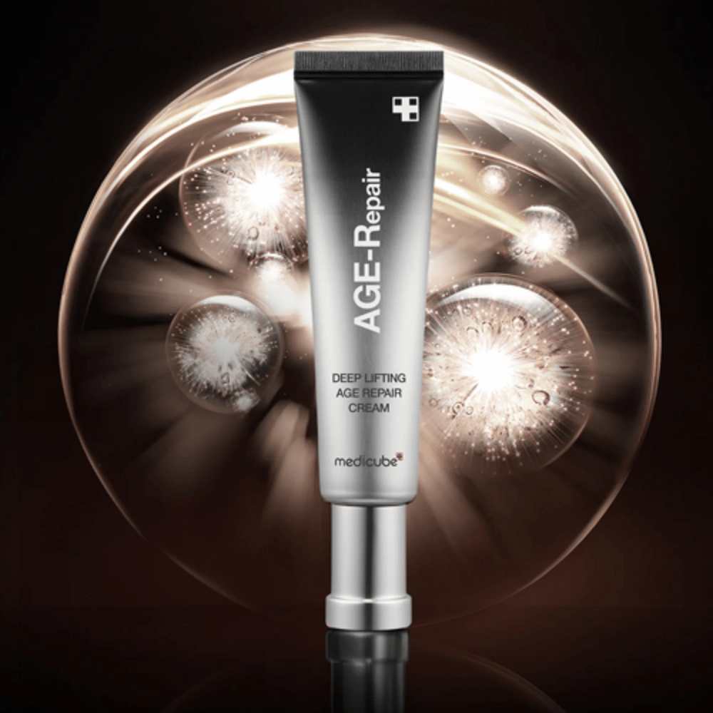 Medicube Deep Lifting Age Repair Cream en tubo plateado sobre fondo con efectos de luz, simboliza anti-envejecimiento y renovación de la piel.