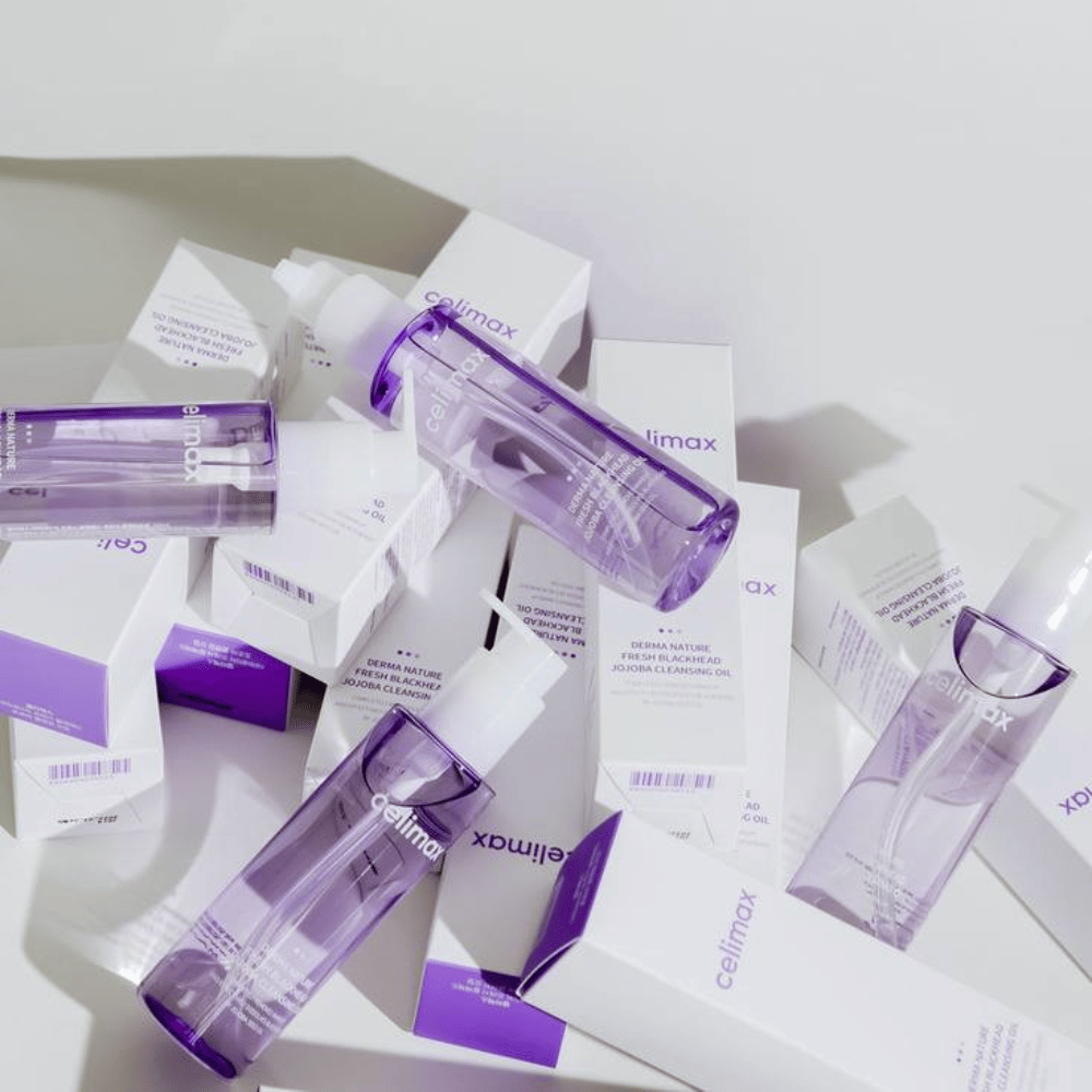 Celimax Derma Nature Fresh Blackhead Jojoba Cleansing Oil en botellas lilas colocadas entre empaques de productos blancos con detalles lilas.