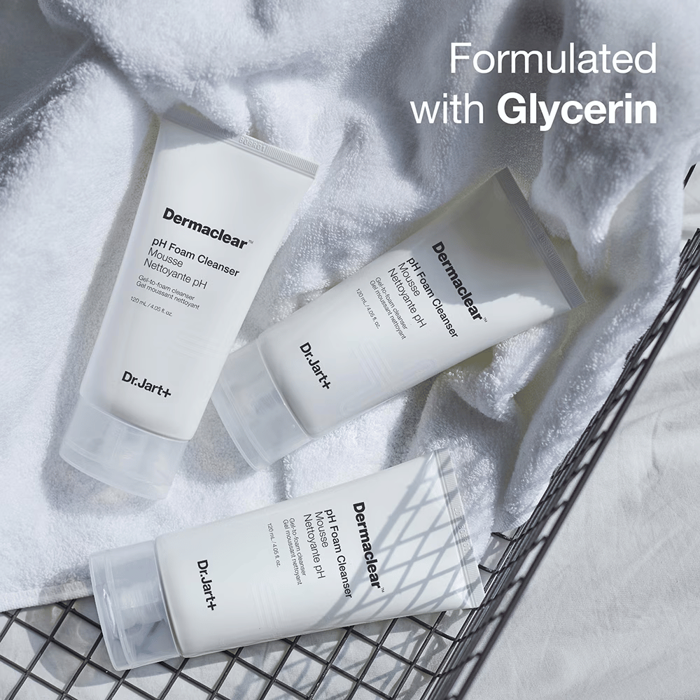 Tres tubos de Dr.Jart+ Dermaclear pH Foam Cleanser están sobre una toalla de felpa blanca en una cesta de metal, con el texto "Formulated with Glycerin" en la esquina superior.