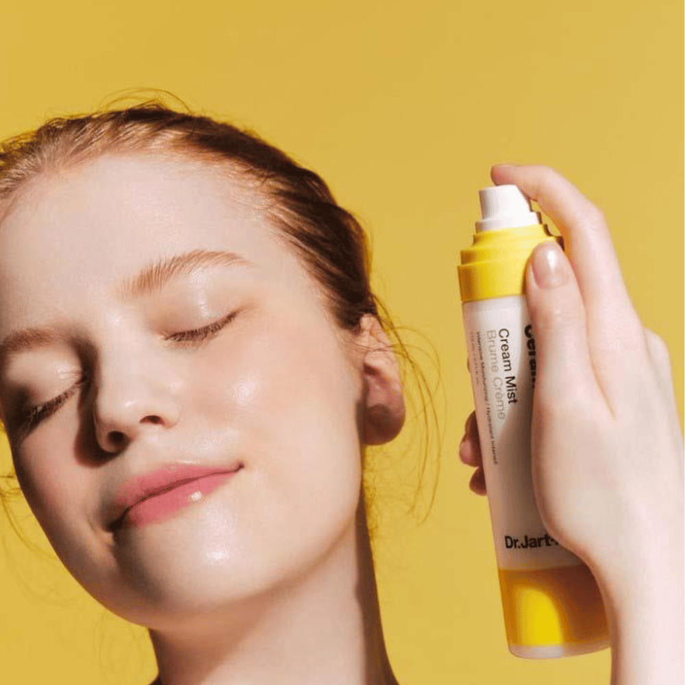 Una mujer sostiene una botella Dr. Jart+ Ceramidin Cream Mist de 110ml en su cara, promoviendo sus beneficios de aumento de humedad y su formulación vegana.