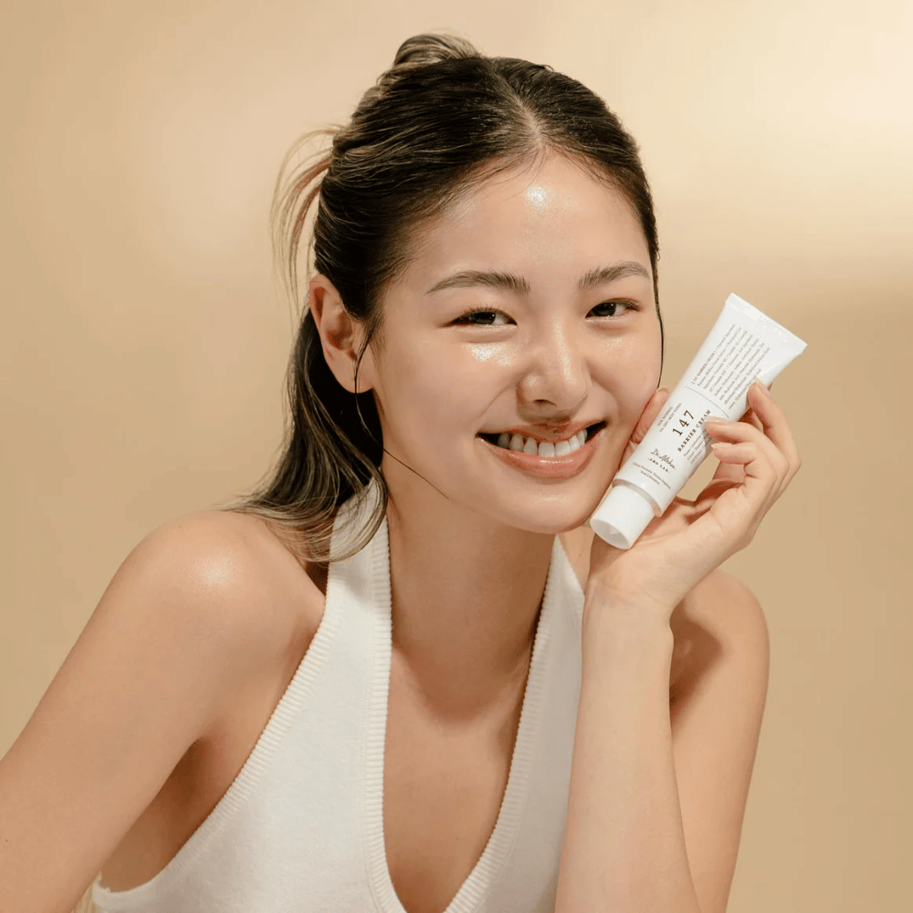 Modelo con piel radiante que sonríe y sostiene Dr. Althea 147 Barrier Cream – una crema facial coreana para la barrera cutánea y la hidratación.