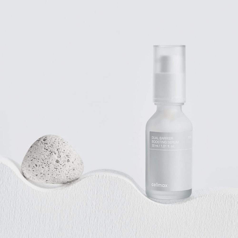 Celimax Dual Barrier Boosting Serum colocado sobre tela con piedra, imagen del producto tranquila que indica hidratación y barrera cutánea fortalecida.