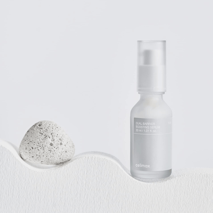 Celimax Dual Barrier Boosting Serum colocado sobre tela con piedra, imagen del producto tranquila que indica hidratación y barrera cutánea fortalecida.