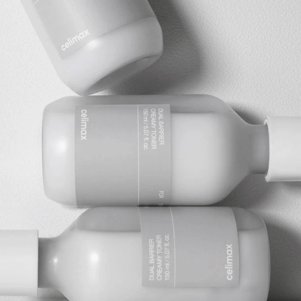 Tres botellas acostadas de Celimax Dual Barrier Creamy Toner en un diseño minimalista con etiqueta gris y luz suave – perfecto para piel sensible y seca.