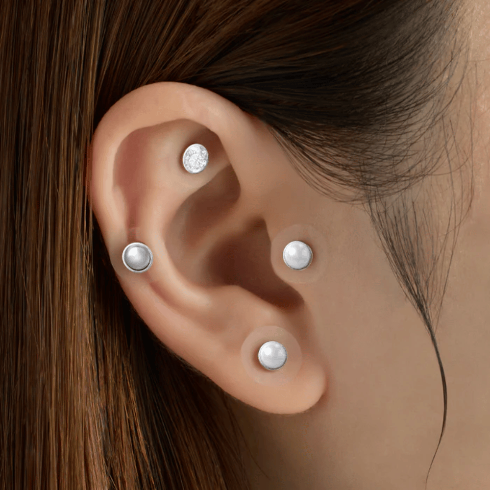 Primer plano de una oreja con varios RETURNITY Ear Therapy Acupressure Patch aplicados en diferentes zonas de la oreja para acupresión y un aspecto elegante.