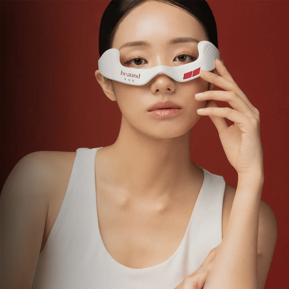 Imagen de modelo donde una persona usa Beaund Eye Rejuv, un dispositivo LED futurista para el área alrededor de los ojos, sobre un elegante fondo rojo.