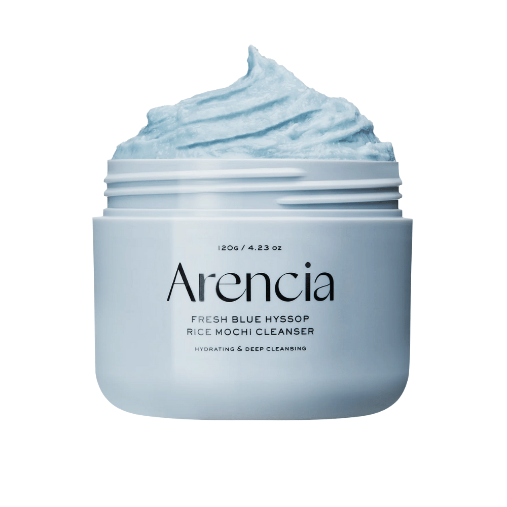 Primer plano de un frasco abierto Arencia Fresh Blue Hyssop Rice Mochi Cleanser. La crema limpiadora azul tiene una textura aireada y batida que llena la parte superior del frasco.