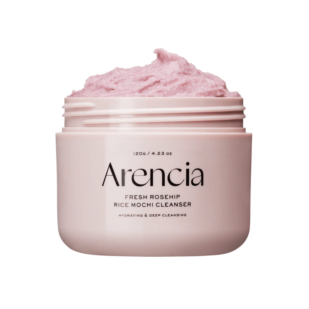 Primer plano de un tarro rosa con Arencia Royal Rosehip Cleanser, lleno de crema limpiadora rosa con textura batida, similar a mochi. El texto en el tarro indica que el producto hidrata y limpia en profundidad.
