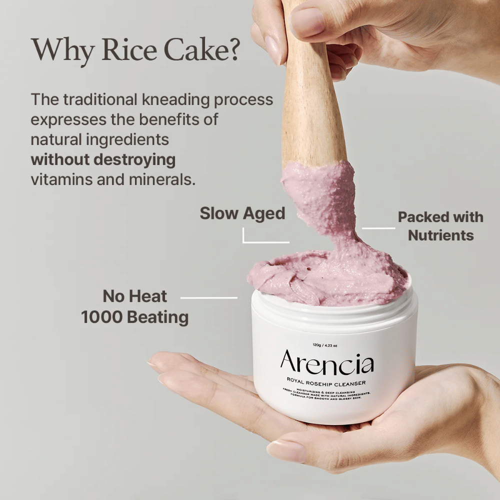 Una mano sostiene un tarro abierto de Arencia Royal Rosehip Cleanser, con una fórmula de limpieza rosa similar a mochi que se levanta con una espátula de madera, mostrando la textura del producto y el método de fabricación tradicional.