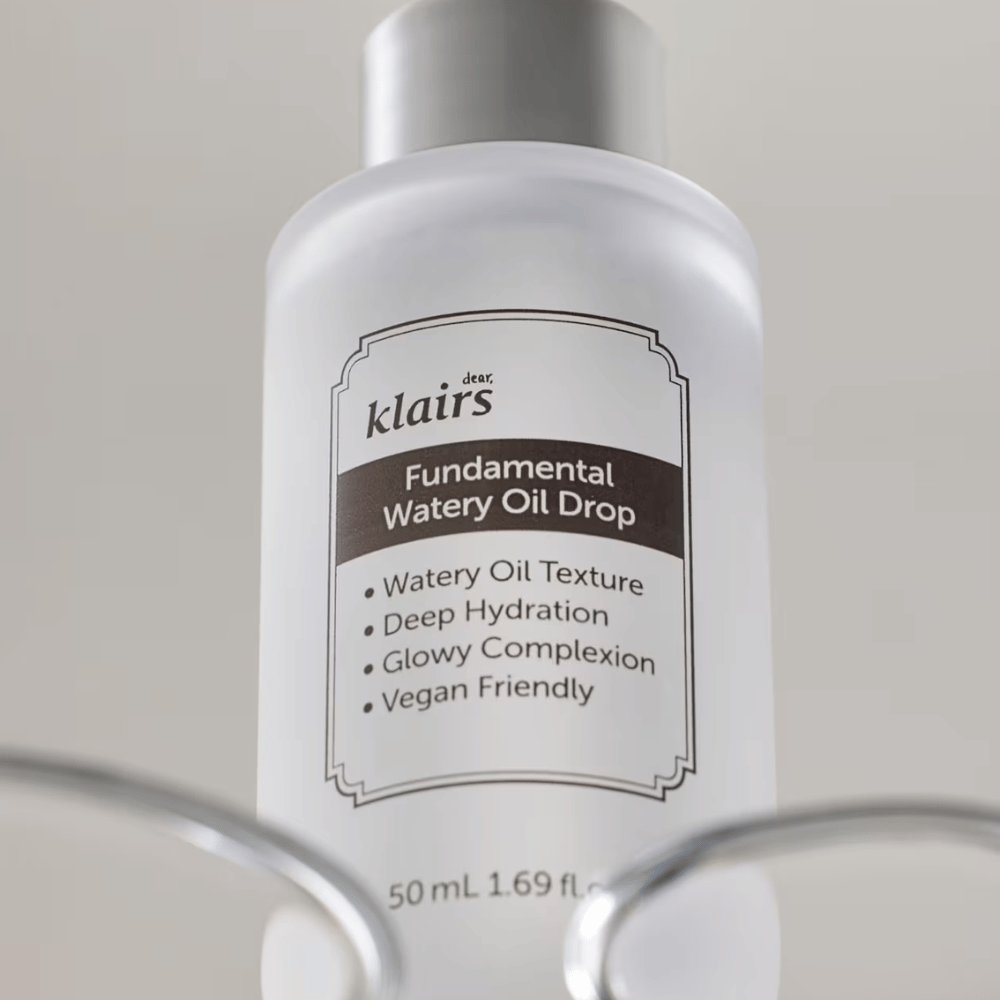 Frasco con Klairs Fundamental Watery Oil Drop, 50 ml, colocado en un soporte transparente, con una etiqueta clara que destaca las propiedades hidratantes y veganas del producto.