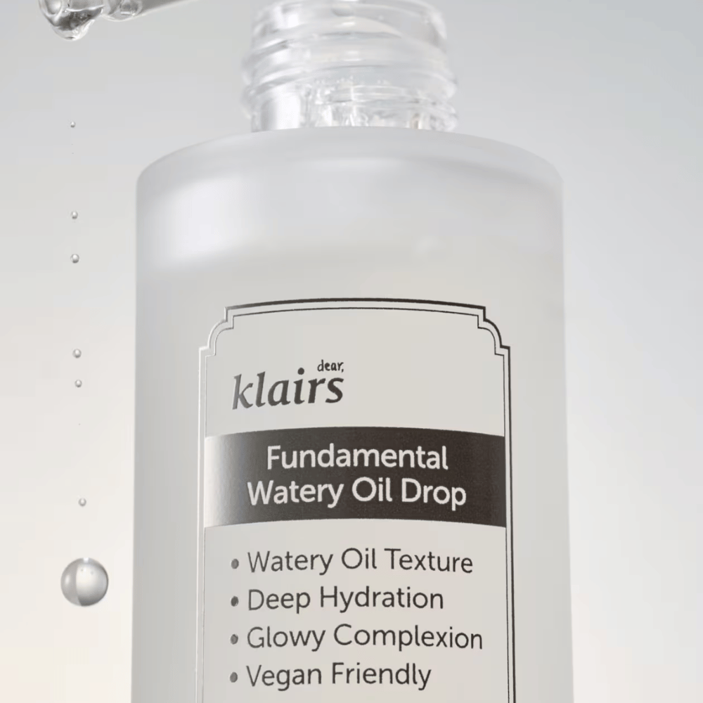 Primer plano del frasco Klairs Fundamental Watery Oil Drop, con texto que destaca las propiedades del producto como "Textura de Aceite Acuoso", "Hidratación Profunda", "Tez Resplandeciente" y "Amigable con los Veganos".