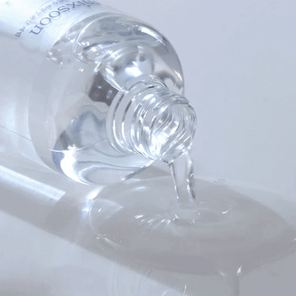 Primer plano de un suero transparente vertiéndose de una botella Mixsoon Glacier Water Hyaluronic Acid Serum sobre una superficie brillante.