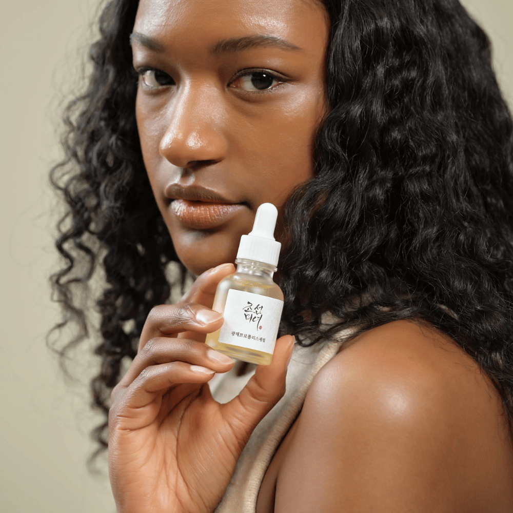Mujer con cabello rizado sostiene una botella de Beauty of Joseon Glow Serum con pipeta, un producto de cuidado de la piel hidratante e iluminador.
