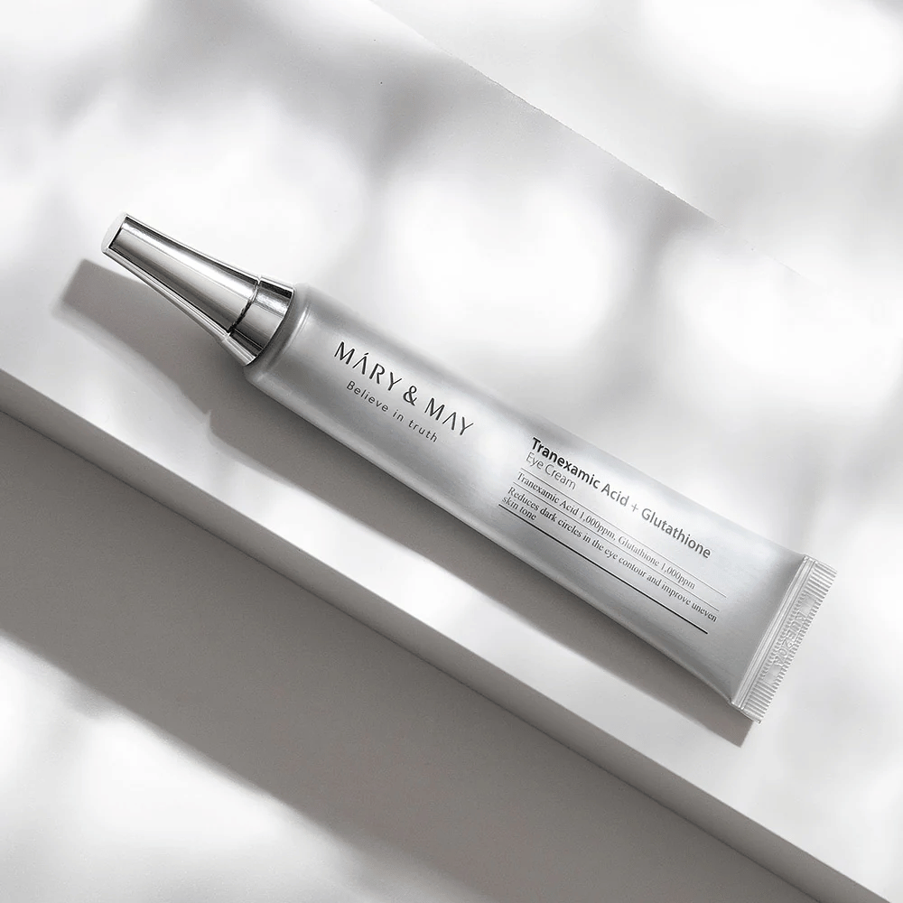 Primer plano de Mary&May Tranexamic Acid + Glutathione Eye Cream con aplicador de metal, desarrollado para aclarar las ojeras y unificar el tono de la piel alrededor de los ojos.