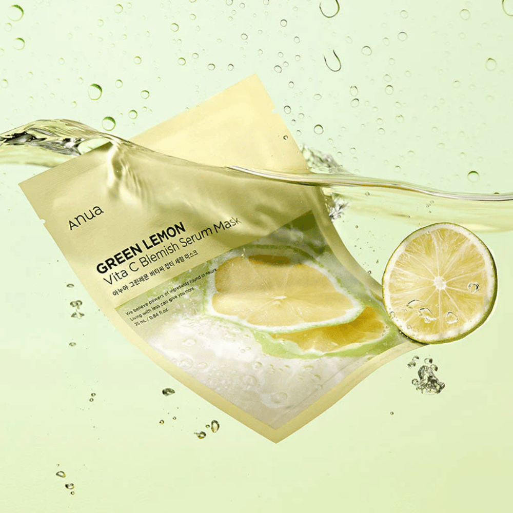 Una imagen vibrante del empaque de Anua Green Lemon Vita C Blemish Serum Mask con gotas de agua transparentes y rodajas de limón verde alrededor. El empaque está parcialmente cubierto por una corriente de agua sobre un fondo verde claro.