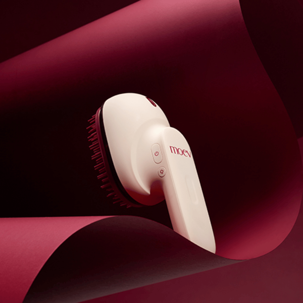 MOEV Hair Steamer Pro en diseño elegante contra un fondo rojo. Cepillo de cuidado capilar innovador que utiliza vapor y calor para dar brillo, suavidad y mejorar la salud del cabello.
