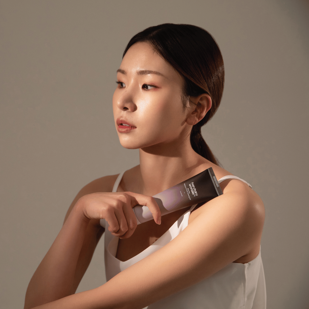 Una joven asiática que sostiene un cepillo en la mano mientras usa Haruharu Wonders Black Rice Moisture 5.5 Soft Cleansing Gel 100ml.