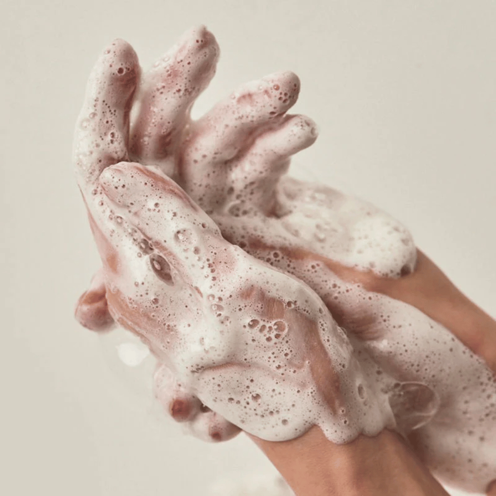 Primer plano de manos cubiertas de una espuma limpiadora rica y cremosa. La imagen ilustra la espuma y las propiedades limpiadoras del producto, además de transmitir claramente la sensación de uso y textura.