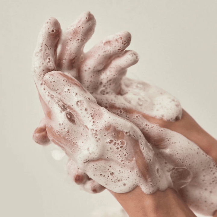 Primer plano de manos cubiertas de una espuma limpiadora rica y cremosa. La imagen ilustra la espuma y las propiedades limpiadoras del producto, además de transmitir claramente la sensación de uso y textura.