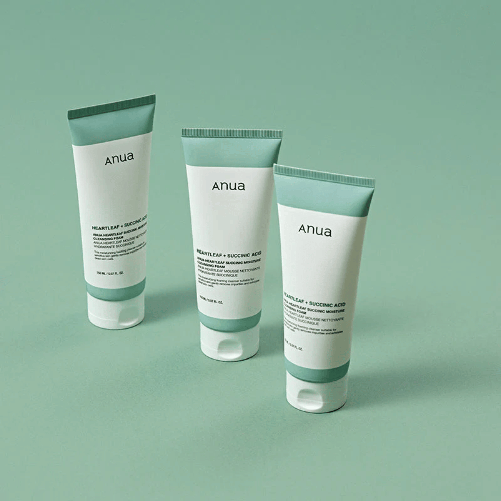 Tres envases de Anua Heartleaf + Succinic Acid Moisture Cleansing Foam presentados sobre un fondo verde claro. La imagen destaca el diseño limpio y minimalista del producto y ofrece una impresión profesional de la línea de productos.