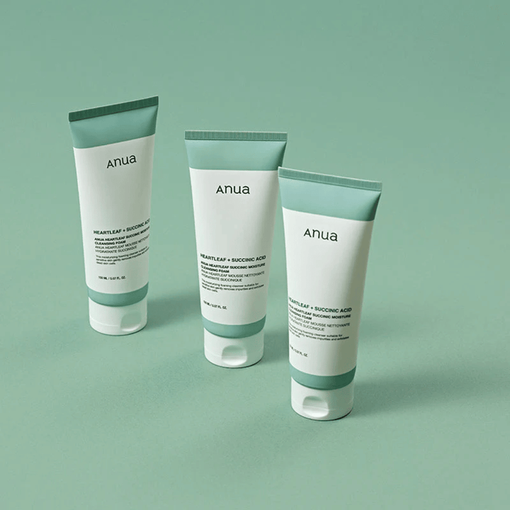 Tres envases de Anua Heartleaf + Succinic Acid Moisture Cleansing Foam presentados sobre un fondo verde claro. La imagen destaca el diseño limpio y minimalista del producto y ofrece una impresión profesional de la línea de productos.