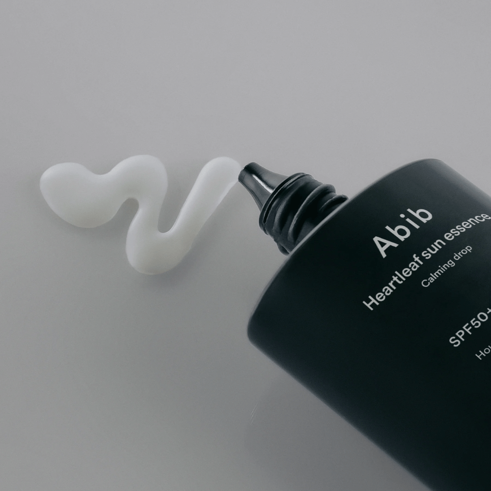 Primer plano de Abib Heartleaf Sun Essence Calming Drop con la crema solar exprimida en una línea blanca y ondulada sobre una superficie clara.