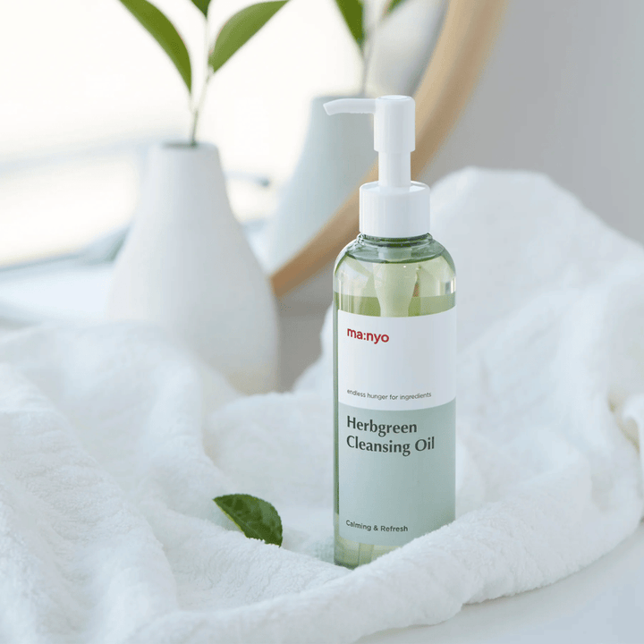 ma:nyo Herbgreen Cleansing Oil en botella con bomba colocada sobre una toalla blanca, aceite limpiador calmante con ingredientes a base de hierbas para una limpieza facial suave