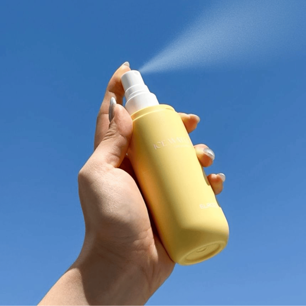 ELROEL Ice Water Sun Mist SPF 40 PA+++ la bruma solar se rocía desde la botella contra un cielo azul, protección solar ligera que hidrata y refresca la piel