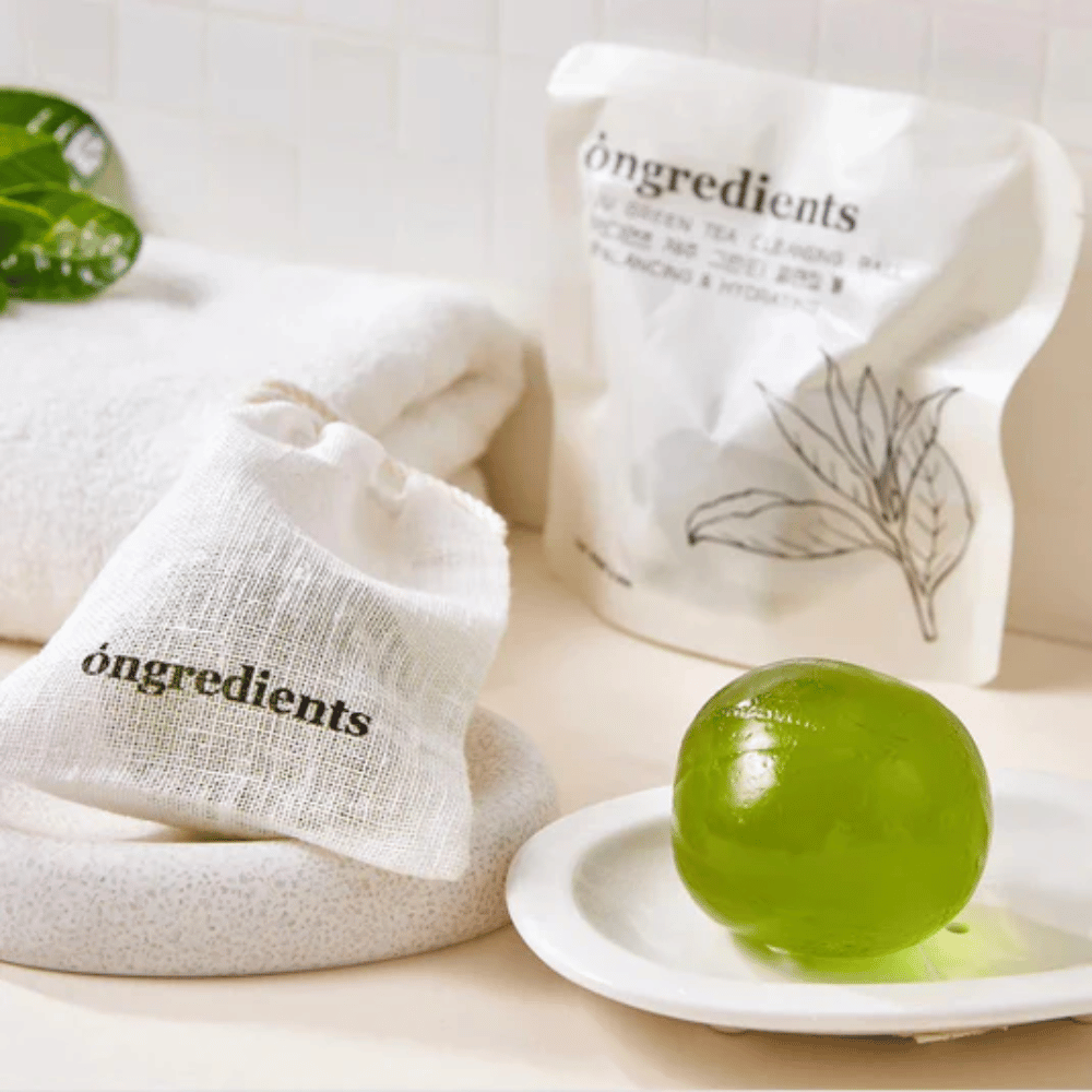 Óngredients Jeju Green Tea Cleansing Ball colocada en un plato con empaque y toalla – limpieza suave con té verde de Jeju.