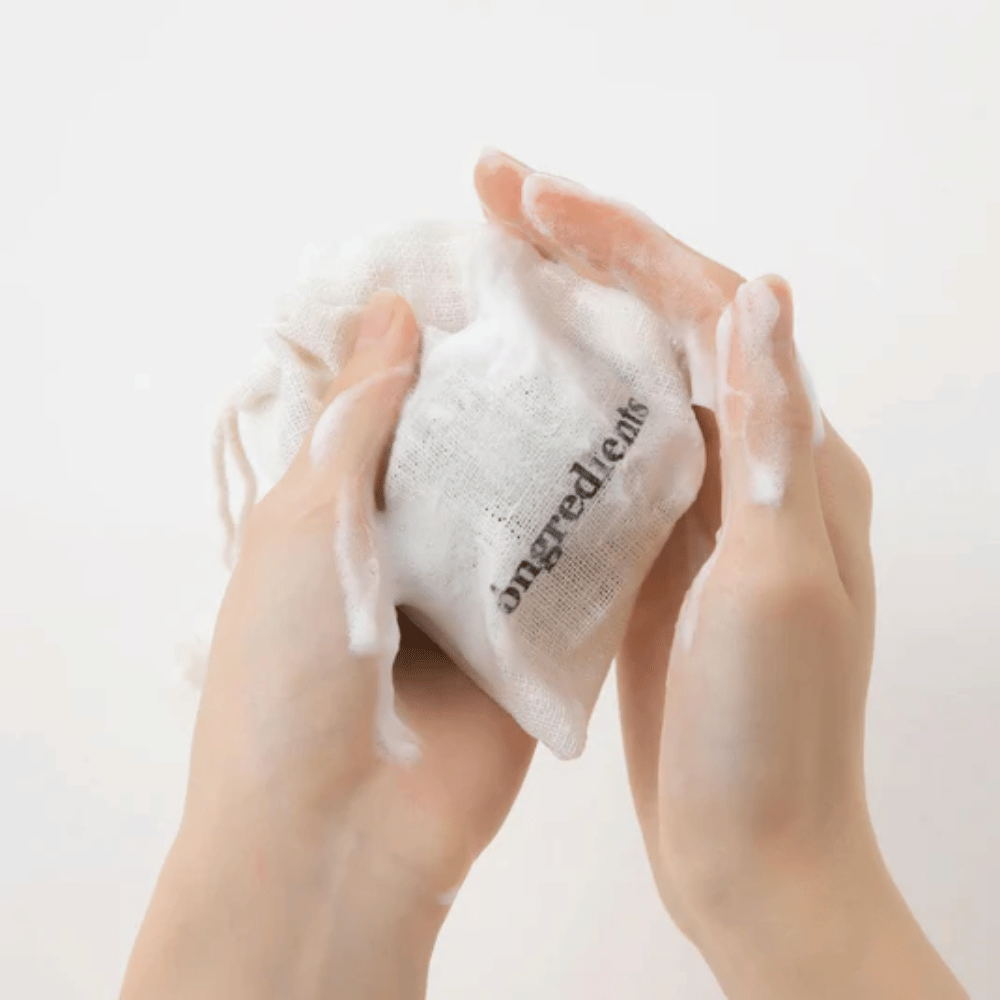 Manos que hacen espuma con Óngredients Jeju Green Tea Cleansing Ball en bolsa de tela – limpieza facial vegana con té verde.