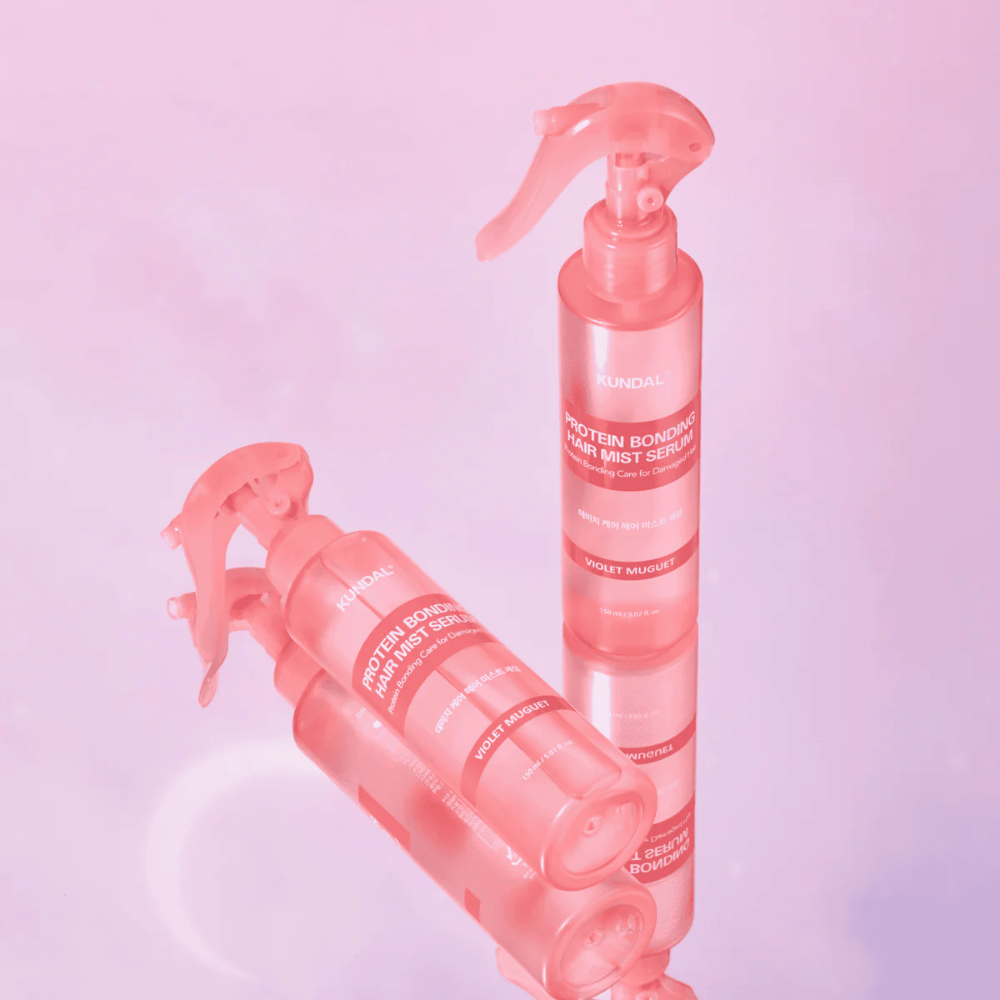 KUNDAL Protein Bonding Hair Mist Serum Violet Muguet en botellas de spray rosas, de pie y acostadas sobre un fondo rosa claro con reflejo.