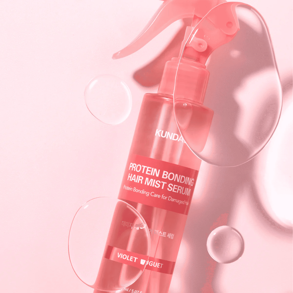 KUNDAL Protein Bonding Hair Mist Serum Violet Bouquet en botella de spray rosa, fotografiada contra un fondo rosa con gotas de agua.