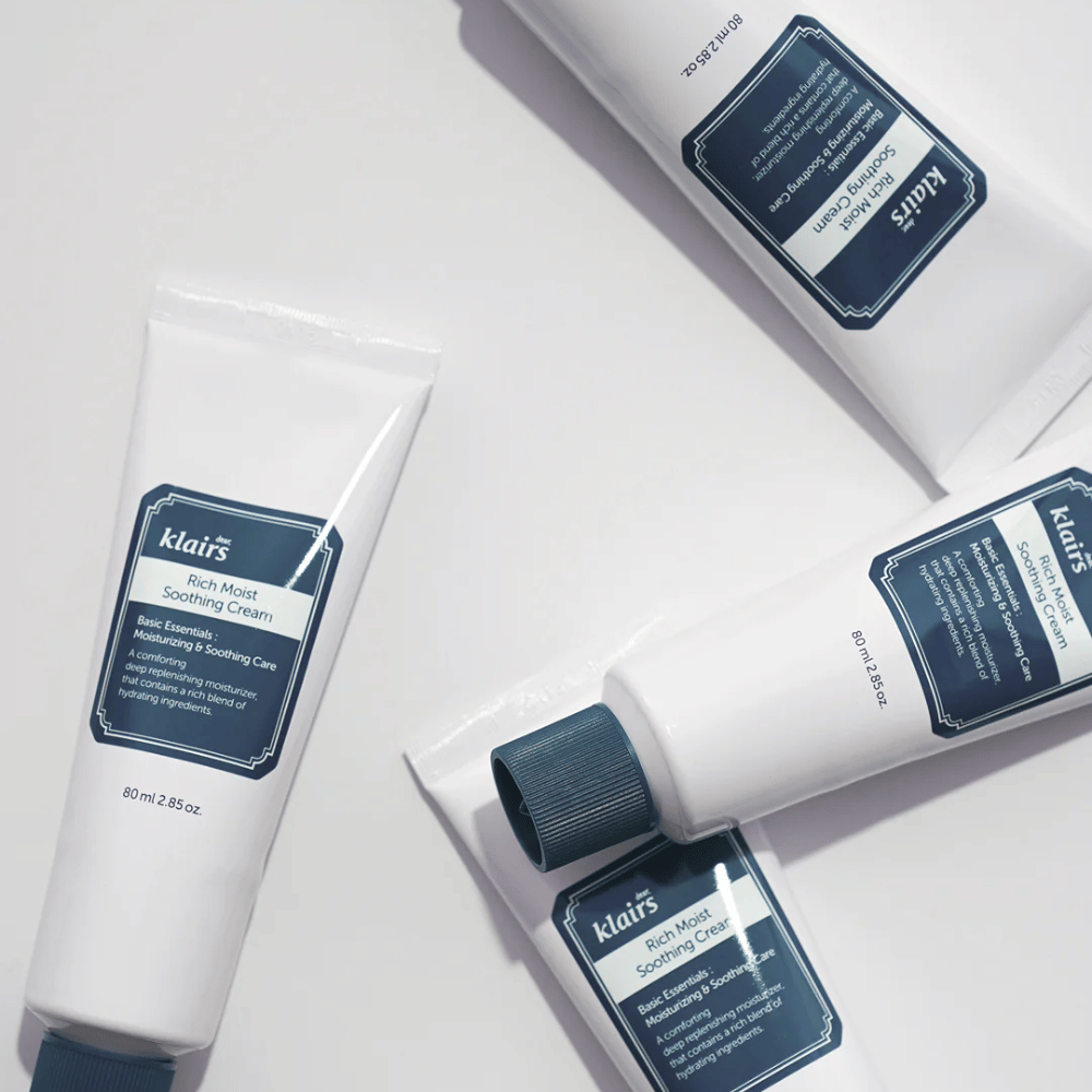 Varios tubos de Klairs Rich Moist Soothing Cream estratégicamente colocados sobre una superficie clara, con sombras que crean profundidad.