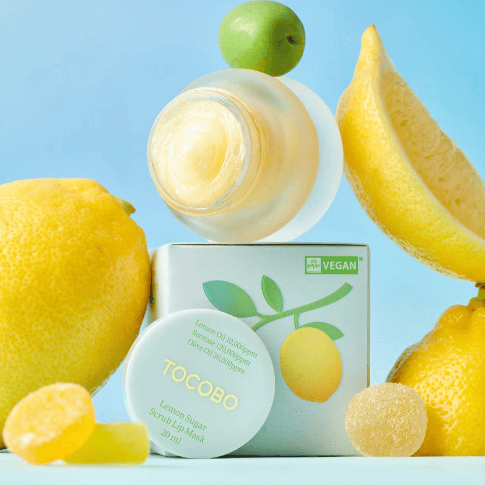 Tarro con Tocobo Lemon Sugar Scrub Lip Mask colocado entre limones y empaque, marcado como apto para veganos.