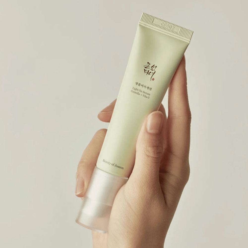 Una mano sostiene Beauty of Joseon Light On Serum con Centella y vitamina C, en un tubo verde claro con diseño minimalista contra un fondo neutral.