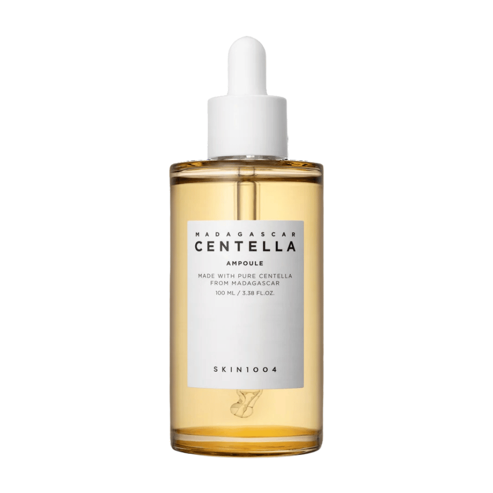 La imagen muestra una botella de "Madagascar Centella Asiatica 100 Ampoule" de SKIN1004. La botella contiene 100 ml y afirma estar hecha con Centella pura de Madagascar. El producto parece ser un suero para el cuidado de la piel y la etiqueta simple da una impresión de pureza y naturalidad. La botella con tapón dosificador sugiere que este es un producto para el cuidado de la piel cuidadosamente dosificado.