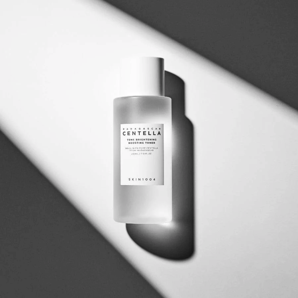 Botella de SKIN1004 Madagascar Centella Tone Brightening Boosting Toner  tumbada sobre una superficie blanca con una sombra dramática en un juego de luces en blanco y negro.