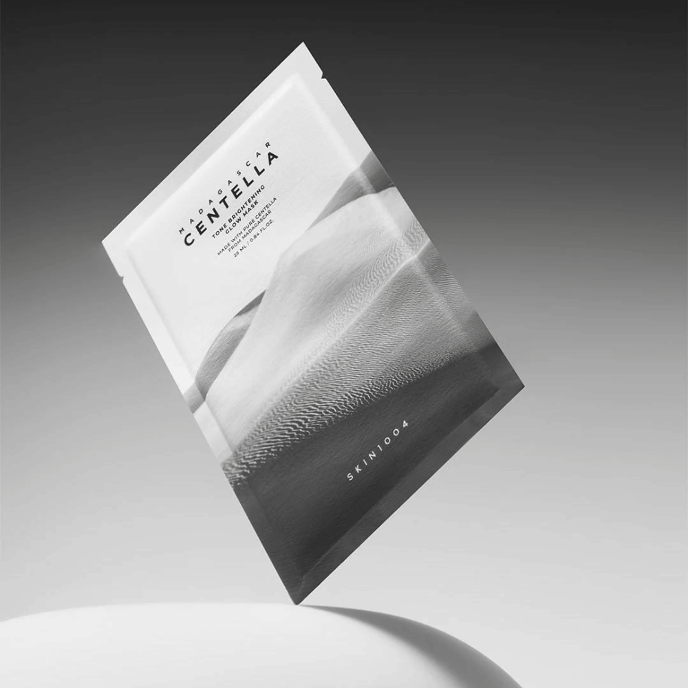 Envase de Sheet mask de SKIN1004 flotando sobre un fondo gris con diseño minimalista.