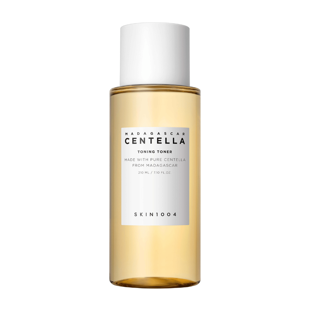 La imagen muestra una botella con tonos de cuidado de la piel, etiquetada "Madagascar Centella Toning Toner" de SKIN1004. Se indica que el producto contiene 210 ml o 7.10 fl.oz y está fabricado con Centella pura de Madagascar. El empaque es sencillo y elegante, con una botella transparente y un líquido de tono dorado en su interior, lo que brinda una sensación de lujo y pureza. El logotipo de la marca SKIN1004 es claramente visible en la parte inferior de la etiqueta.