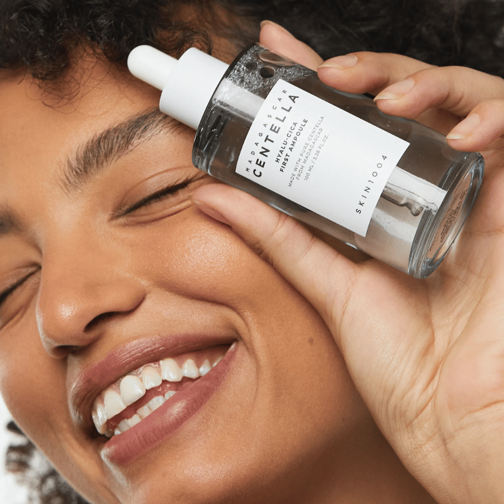 Mujer sonriente sostiene Skin1004 Madagascar Centella Hyalu-Cica First Ampoule junto a su cara.
