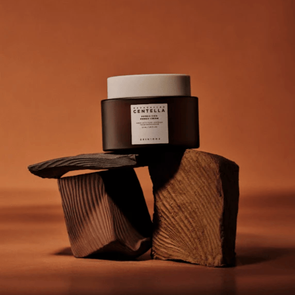 SKIN1004 Madagascar Centella Probio-Cica Enrich Cream en elegante frasco de vidrio marrón sobre bloques de madera decorativos - crema facial coreana nutritiva que fortalece la barrera de la piel.