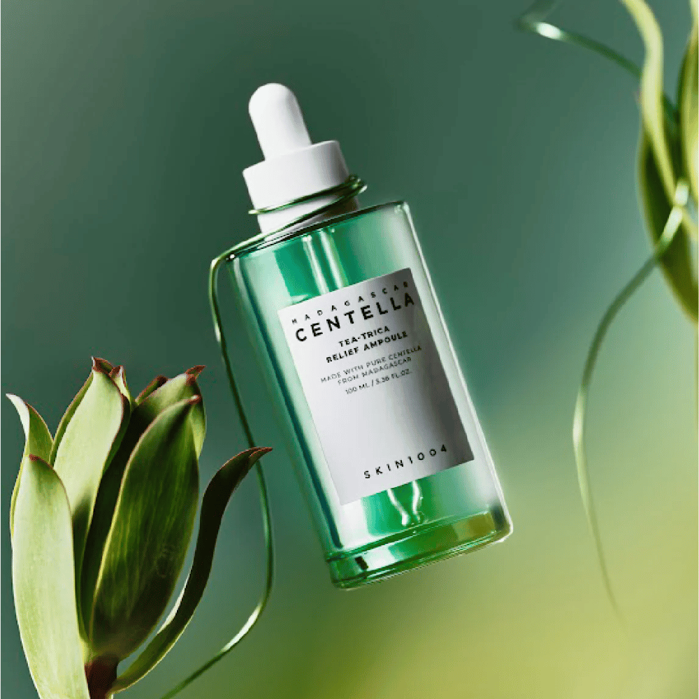 SKIN1004 Madagascar Centella Tea-Trica Relief Ampoule – botella de vidrio verde con pipeta, etiqueta blanca y 100 ml de contenido, fotografiada contra un fondo verde con detalles de plantas.